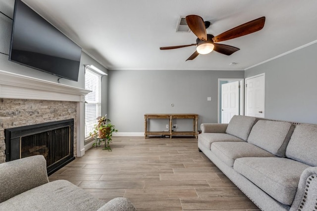 living room featuring a stone fireplace, baseboards, light wood finished floors, and ornamental molding