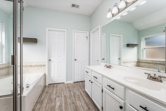 bathroom featuring visible vents, lofted ceiling, wood finished floors, a bath, and a sink