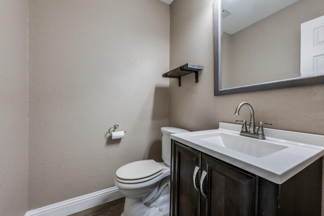 bathroom featuring vanity, wood finished floors, baseboards, toilet, and a textured wall