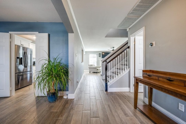 hallway with light wood-style flooring, stairs, and baseboards