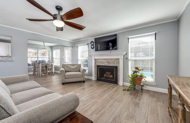 living room with baseboards, a fireplace, ceiling fan, crown molding, and light wood-type flooring