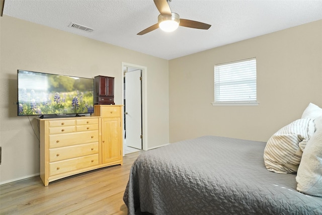 bedroom with ceiling fan, light wood-style flooring, visible vents, and a textured ceiling