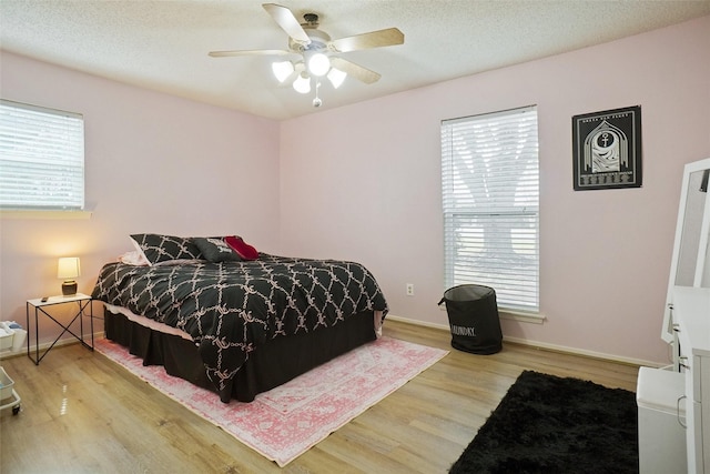 bedroom with ceiling fan, wood finished floors, baseboards, and a textured ceiling