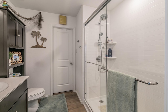 bathroom with a stall shower, toilet, vanity, and wood finished floors