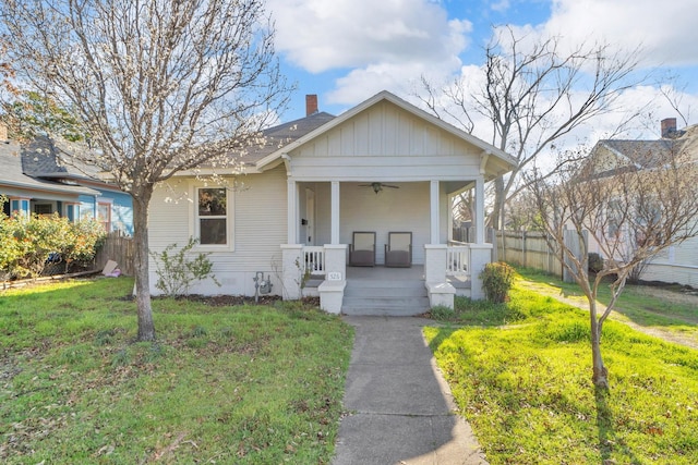 bungalow-style house with a front yard, fence, a porch, ceiling fan, and board and batten siding