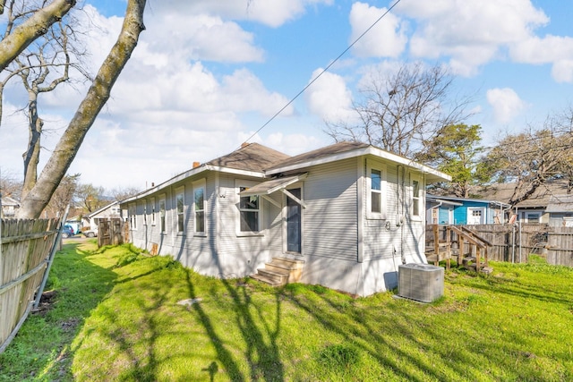 back of property with a yard, entry steps, central AC, and fence