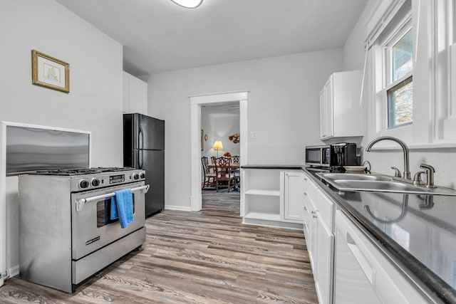 kitchen with dark countertops, light wood-type flooring, appliances with stainless steel finishes, white cabinetry, and a sink