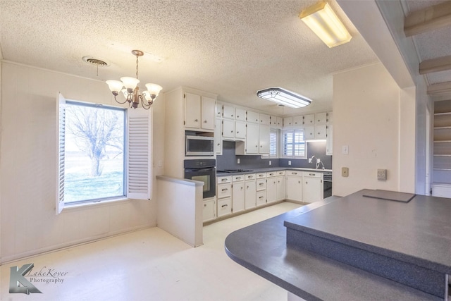 kitchen featuring stainless steel microwave, black oven, light floors, a notable chandelier, and a sink