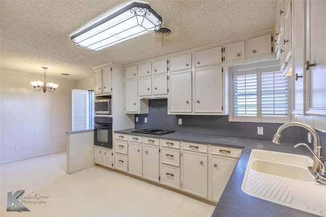 kitchen with a sink, black appliances, white cabinets, dark countertops, and a notable chandelier