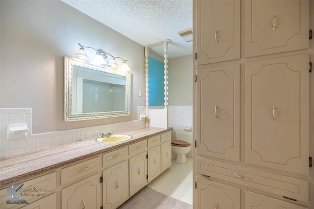 bathroom with toilet, a textured ceiling, tile walls, wainscoting, and vanity