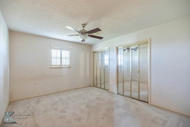 unfurnished bedroom featuring carpet flooring, a ceiling fan, multiple closets, and a textured ceiling