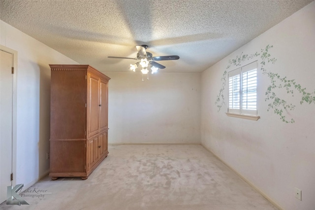 empty room featuring baseboards, light colored carpet, a ceiling fan, and a textured ceiling