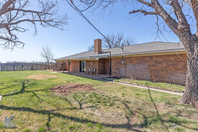 back of property featuring a patio, fence, a yard, brick siding, and a chimney