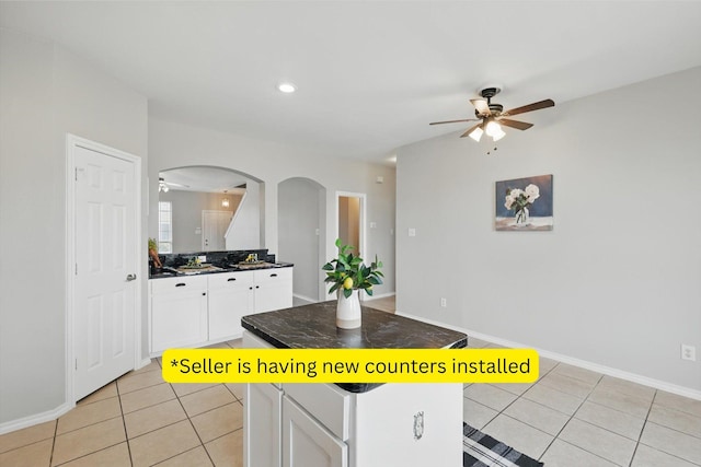 kitchen with white cabinets, light tile patterned floors, arched walkways, and a kitchen island