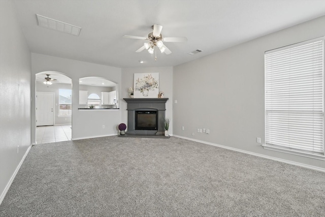 unfurnished living room with visible vents, light carpet, arched walkways, a glass covered fireplace, and a ceiling fan