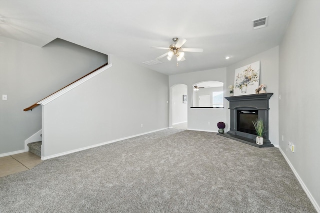 unfurnished living room with arched walkways, stairway, carpet flooring, and a glass covered fireplace