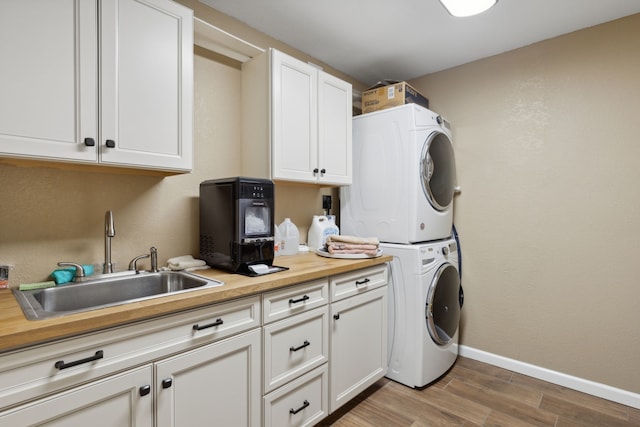 laundry area featuring wood finished floors, baseboards, cabinet space, a sink, and stacked washer / drying machine