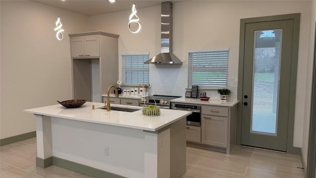 kitchen featuring appliances with stainless steel finishes, gray cabinetry, wall chimney range hood, and a sink