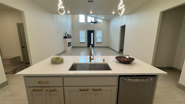 kitchen featuring a kitchen island with sink, a sink, stainless steel dishwasher, open floor plan, and a fireplace