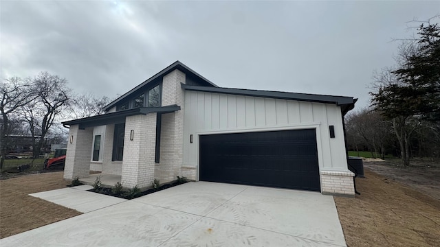 view of home's exterior featuring driveway, central AC, board and batten siding, a garage, and brick siding