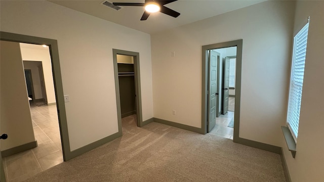 unfurnished bedroom with visible vents, a walk in closet, baseboards, light colored carpet, and a ceiling fan