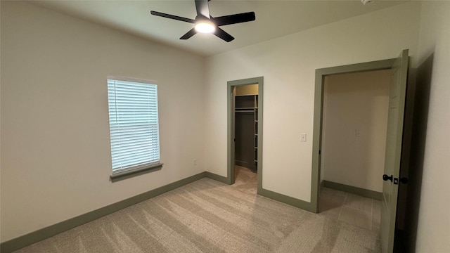 unfurnished bedroom featuring a ceiling fan, baseboards, a closet, light carpet, and a walk in closet