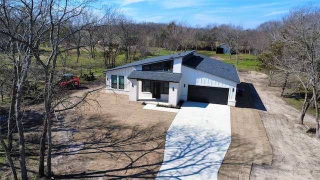 view of front of house featuring brick siding, a wooded view, an attached garage, roof with shingles, and driveway