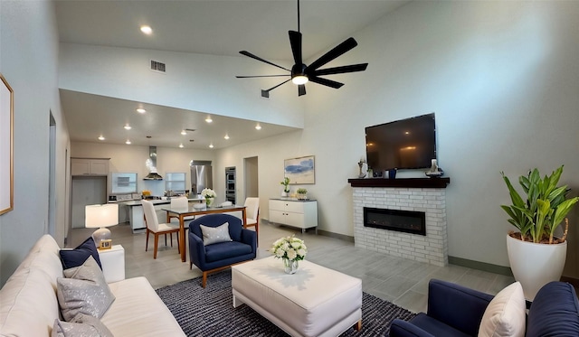 living area with visible vents, baseboards, ceiling fan, a fireplace, and a high ceiling