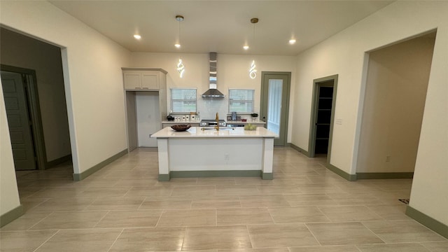 kitchen featuring a kitchen island with sink, recessed lighting, wall chimney range hood, baseboards, and light countertops