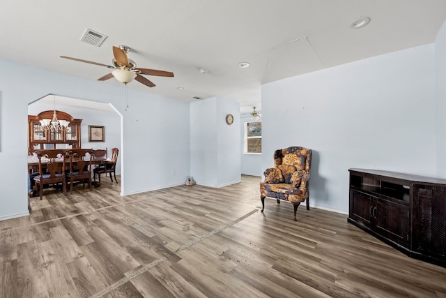 sitting room featuring ceiling fan with notable chandelier, wood finished floors, visible vents, and arched walkways