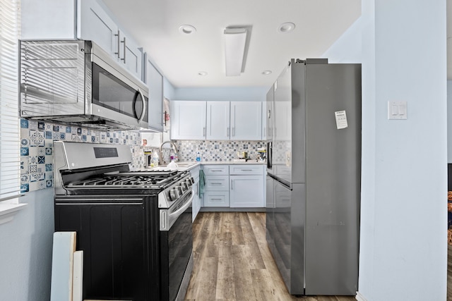 kitchen with light wood-style flooring, a sink, stainless steel appliances, white cabinets, and backsplash