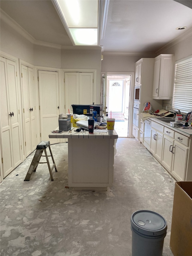 kitchen with oven, ornamental molding, tile counters, concrete flooring, and white cabinetry