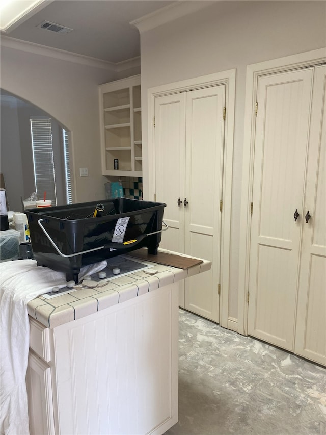 kitchen with visible vents, tile countertops, ornamental molding, arched walkways, and open shelves