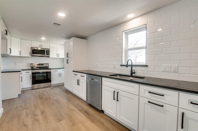 kitchen with dark countertops, visible vents, light wood-style floors, stainless steel appliances, and a sink