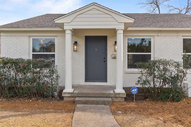 view of exterior entry with brick siding and a shingled roof