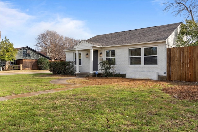 view of front of property with brick siding, roof with shingles, a front lawn, and fence