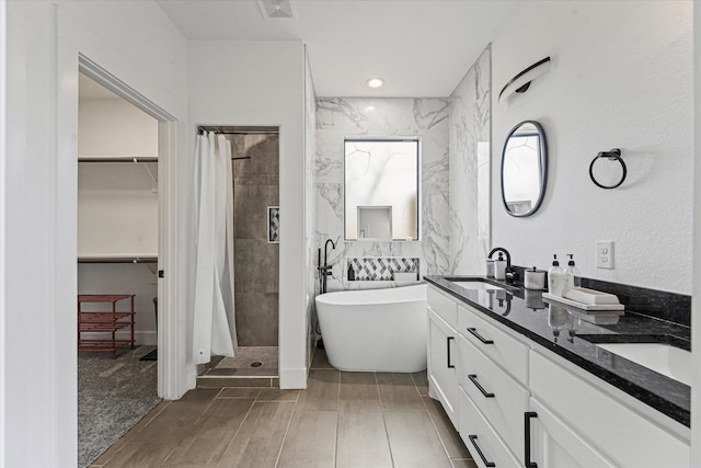 full bath featuring a shower stall, a freestanding tub, tile walls, and a sink