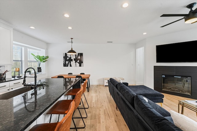 living area featuring recessed lighting, light wood-style flooring, a ceiling fan, and a glass covered fireplace