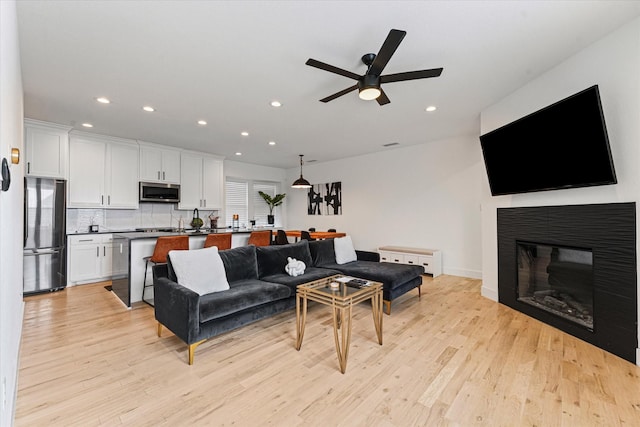 living room featuring recessed lighting, a glass covered fireplace, a ceiling fan, and light wood finished floors