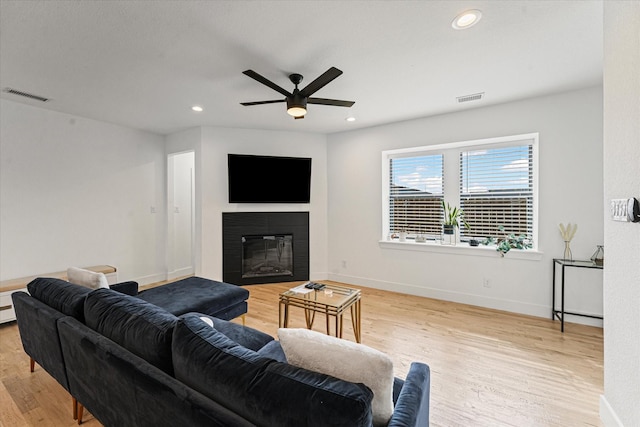 living room featuring light wood-type flooring, visible vents, a glass covered fireplace, and recessed lighting