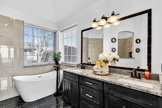 full bathroom featuring double vanity, vaulted ceiling, a freestanding tub, and a sink