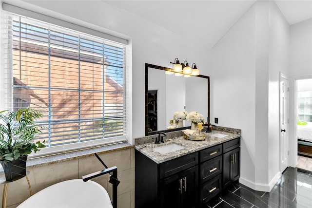 bathroom with double vanity, connected bathroom, a freestanding bath, and a sink