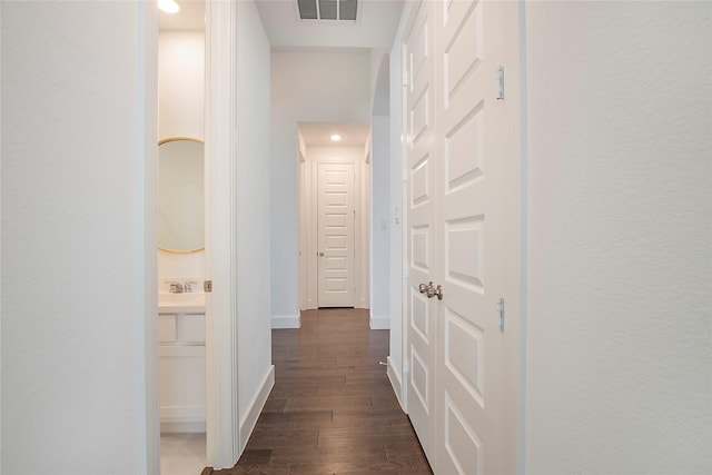 corridor with a sink, visible vents, baseboards, and dark wood-style floors