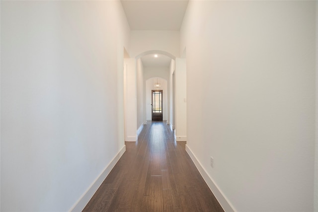 hall with dark wood-type flooring, baseboards, and arched walkways