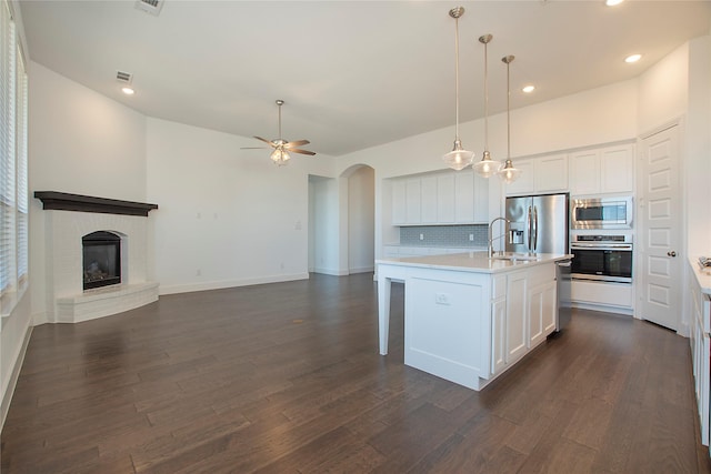 kitchen with a fireplace, arched walkways, ceiling fan, appliances with stainless steel finishes, and backsplash