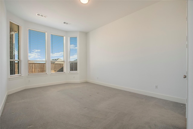 empty room featuring baseboards, visible vents, and light carpet