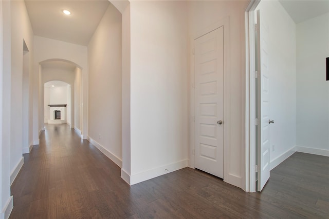 hall featuring dark wood-type flooring, recessed lighting, arched walkways, and baseboards