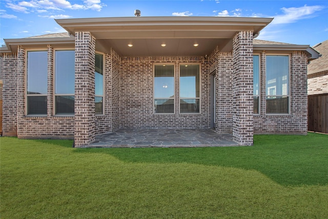 back of property with a yard, a patio, brick siding, and fence