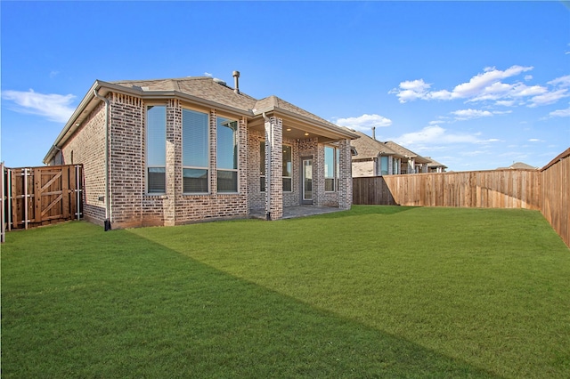 rear view of property with a yard, brick siding, and a fenced backyard