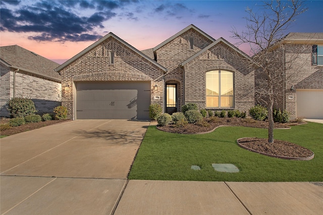 french country style house featuring brick siding, a lawn, an attached garage, and concrete driveway